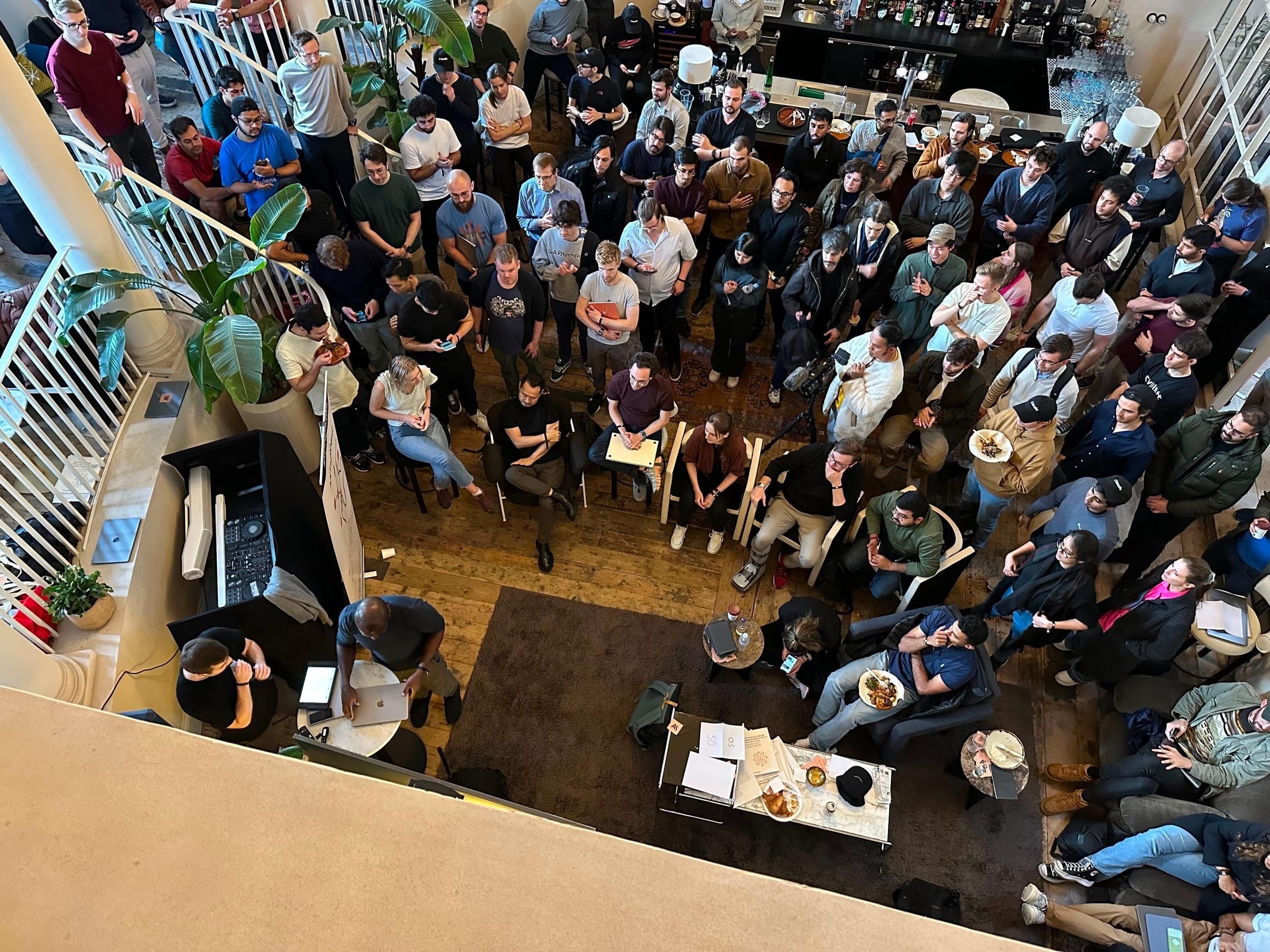 A spacious room filled with people, gathered and listening to a speaker from an elevated position.